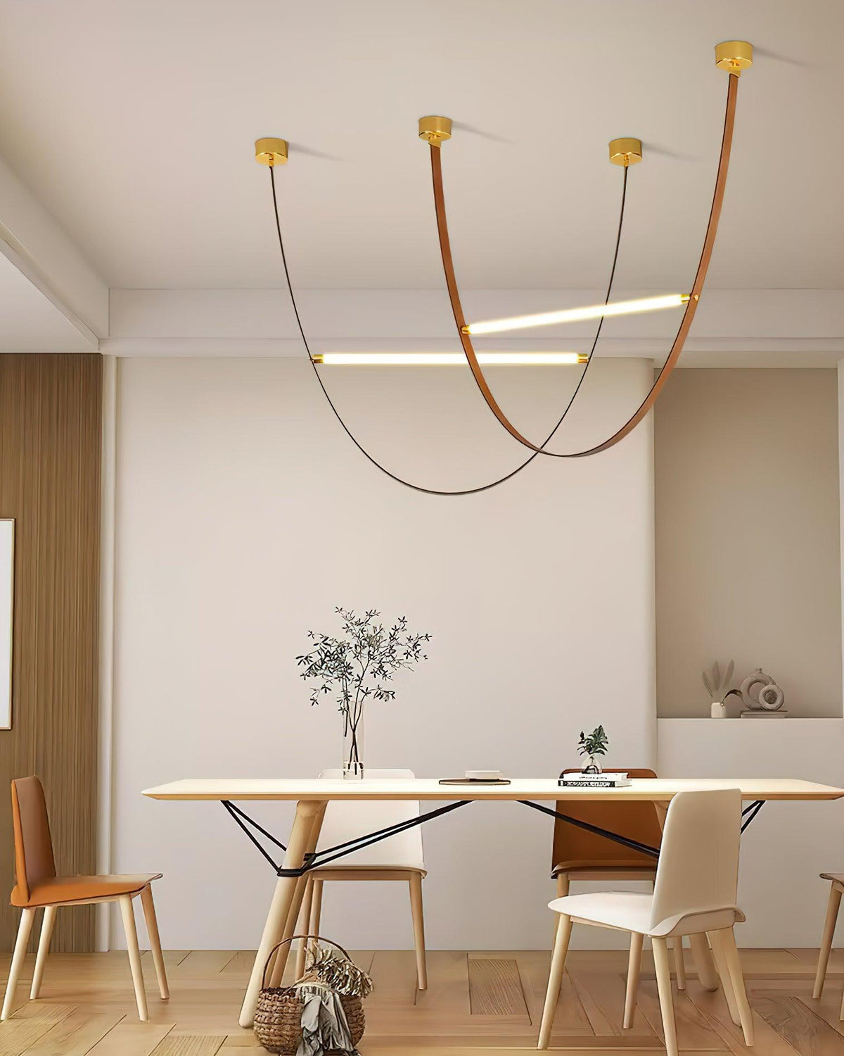Three leather loops and two crossing light bars hang over a long dining table with wooden chairs, on this Clérachic pendant.