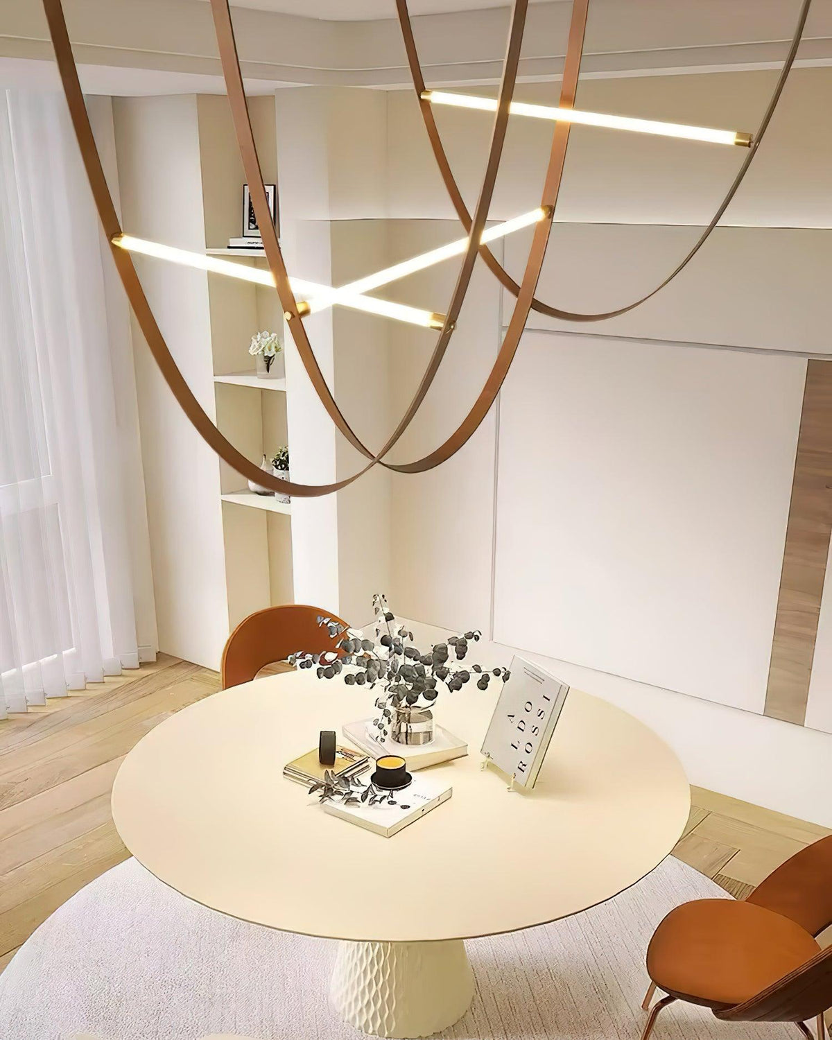 Tall view of leather straps and glowing bars from this Clérachic pendant above a round cream table in a room with shelving.