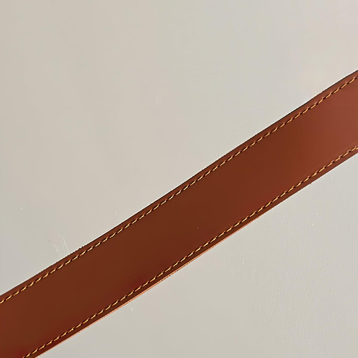 Close view of the stitched edge on a tan leather strap from this Clérachic pendant, against a pale wall.