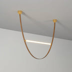 Single tan leather loop with a lit bar across it, hung from two brass canopy plates against a grey wall, on this Clérachic pendant.