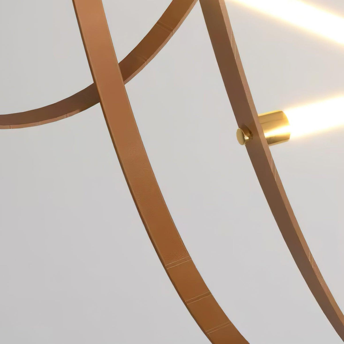 Close view of two tan leather straps and a brass clamp holding the lit end of a light bar on this Clérachic pendant.