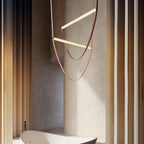 Two angled light bars on tan leather loops from this Clérachic pendant, set against a curved beige wall near a freestanding bath.