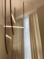 Light bars glowing between tall cream curtains and a high ceiling, three leather loops of this Clérachic pendant hanging from above.