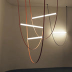Three bright bars on copper-toned leather loops, with a black loop beside them, on this Clérachic pendant against a dark wall.
