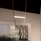 A single leather loop and one lit bar from this Clérachic pendant, hung in a showroom with a dark ceiling and a crystal display behind.