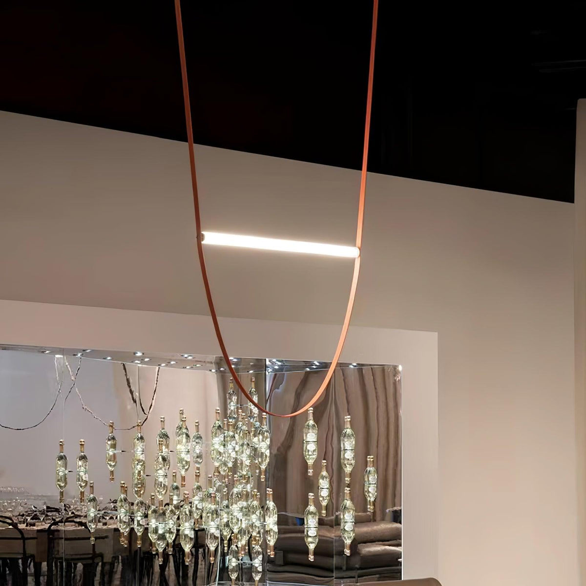 A single leather loop and one lit bar from this Clérachic pendant, hung in a showroom with a dark ceiling and a crystal display behind.
