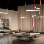 This Clérachic pendant hangs in front of cream drapes in a lounge with low grey sofas and a dark concrete floor.