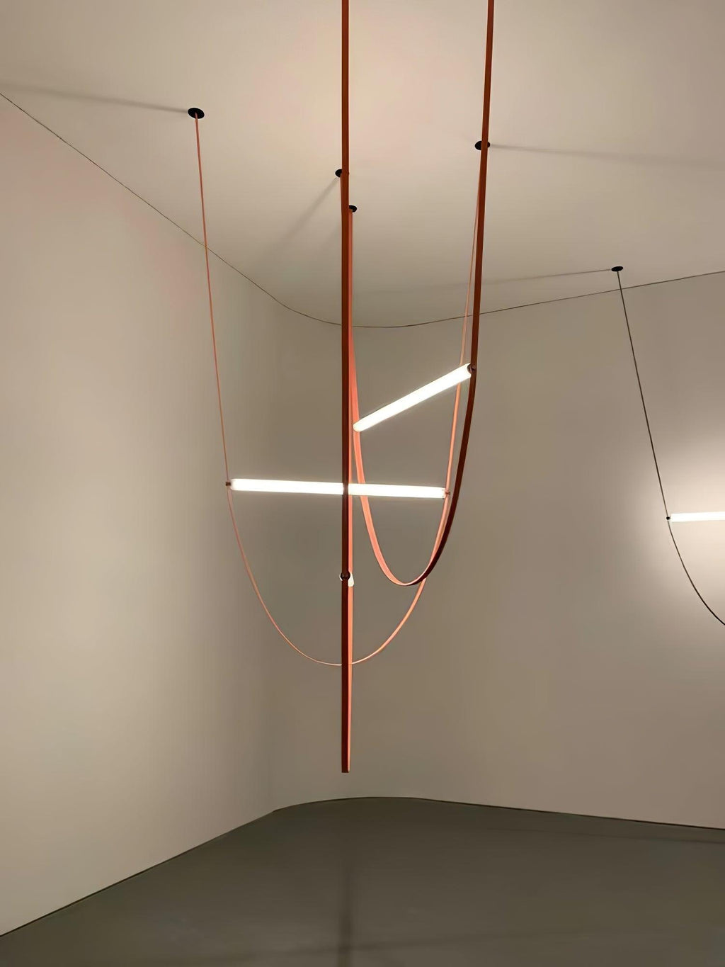Leather loops and three light bars from this Clérachic pendant hang in the corner of a bare room with a polished floor.