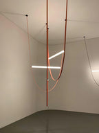 Leather loops and three light bars from this Clérachic pendant hang in the corner of a bare room with a polished floor.