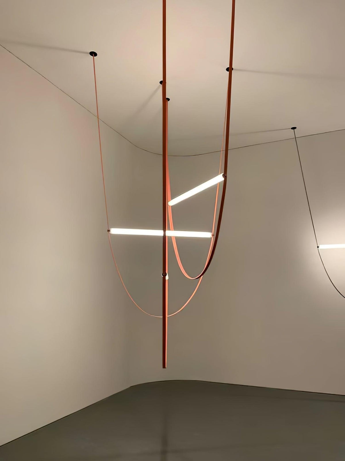 Leather loops and three light bars from this Clérachic pendant hang in the corner of a bare room with a polished floor.