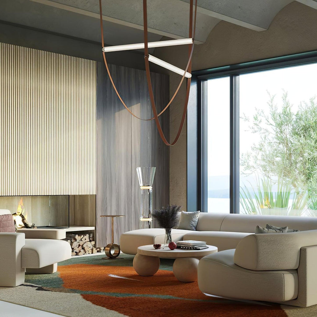 A Clérachic pendant with light bars on tan leather loops hanging over a cream sofa, in a room with a fluted wall and large window.