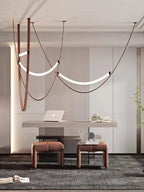 Curved light bars on leather loops hang over a pale desk and two low stools, in a room lit by this Clérachic pendant.