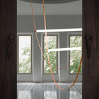 Light bars on leather loops from this Clérachic pendant seen between two dark carved wooden posts, with trees outside the windows.
