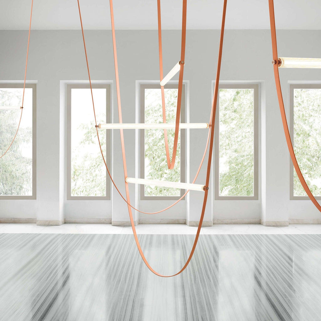 Light bars and tan leather loops from this Clérachic pendant in a white room with tall windows and a polished stone floor.