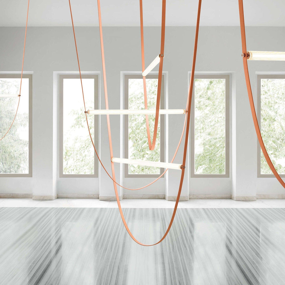 Light bars and tan leather loops from this Clérachic pendant in a white room with tall windows and a polished stone floor.