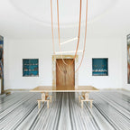 A Clérachic pendant with three leather loops hangs in a round white room with a wooden door and a long stone-topped table.