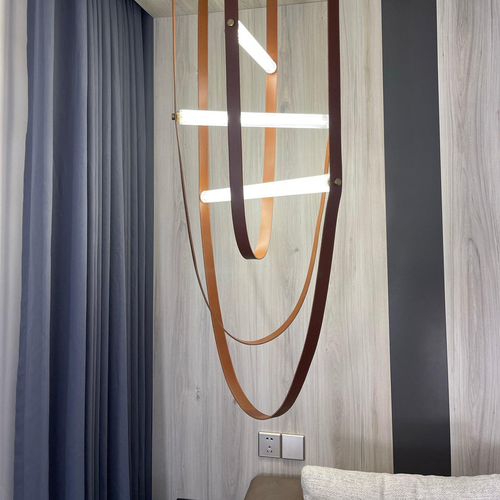 Leather loops and angled light bars from this Clérachic pendant hang against a grey wall and striped blue curtain.