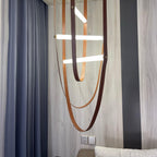 Leather loops and angled light bars from this Clérachic pendant hang against a grey wall and striped blue curtain.