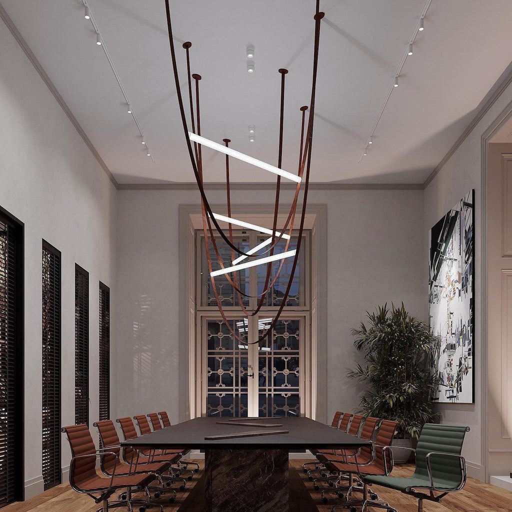 A Clérachic pendant with dark leather loops hung above a long table in a room lit by wall-mounted tracks.