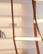 Close view of a lit bar with a ribbed glass tube and brass cap on tan leather, on this Clérachic pendant, with shelves behind.