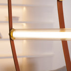 Close view of a ribbed glass light tube held in a brass cap between two stitched leather straps on this Clérachic pendant.