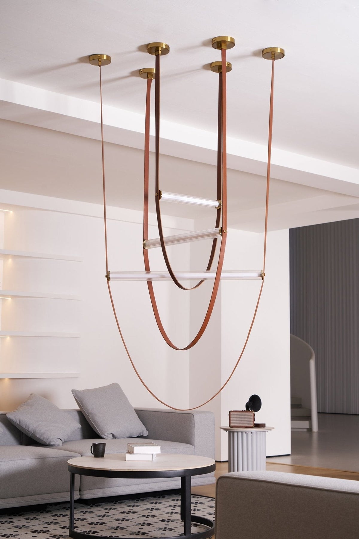 This Clérachic pendant hung in a pale living room, its leather loops and unlit bars reaching down past a coffee table and sofa.