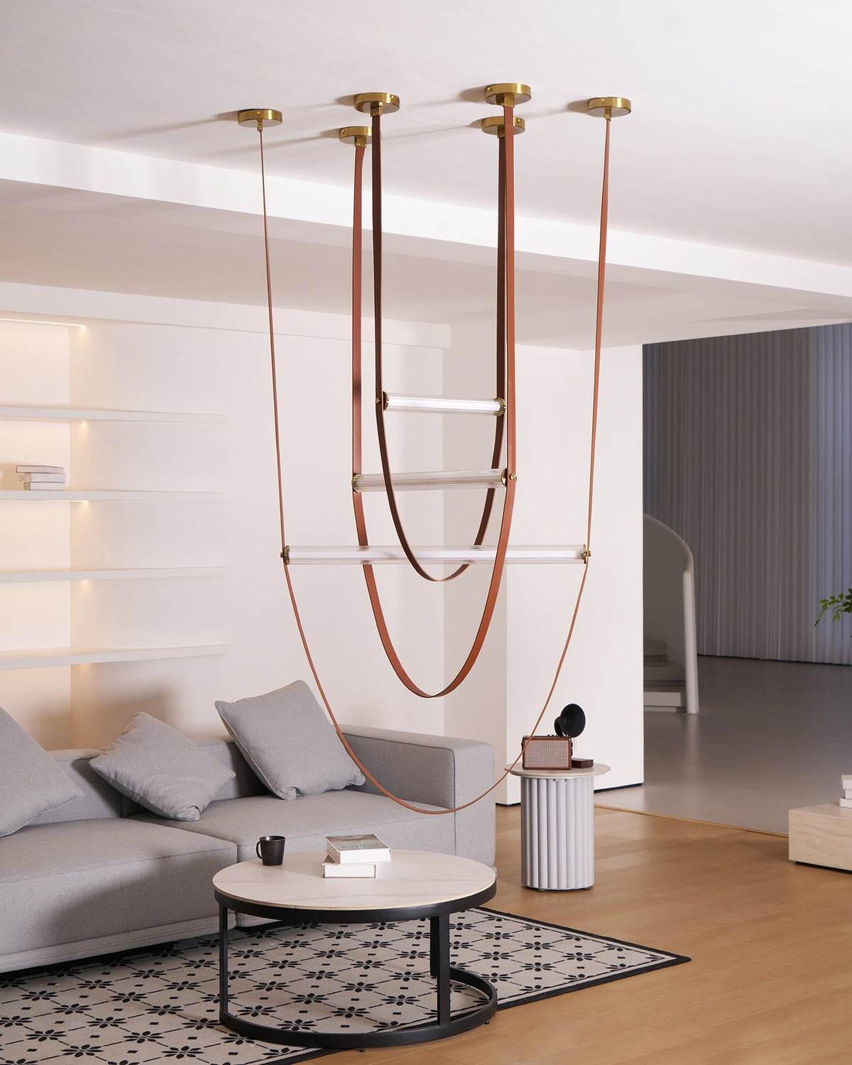 Wide view of this Clérachic pendant with leather loops and bars switched off, a round coffee table and sofa below.
