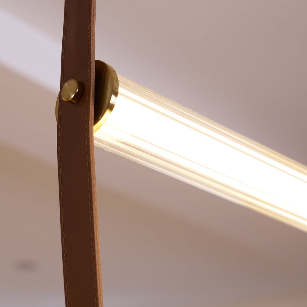 Close view of a brass button fixing a leather strap to the glowing ribbed tube of this Clérachic pendant.