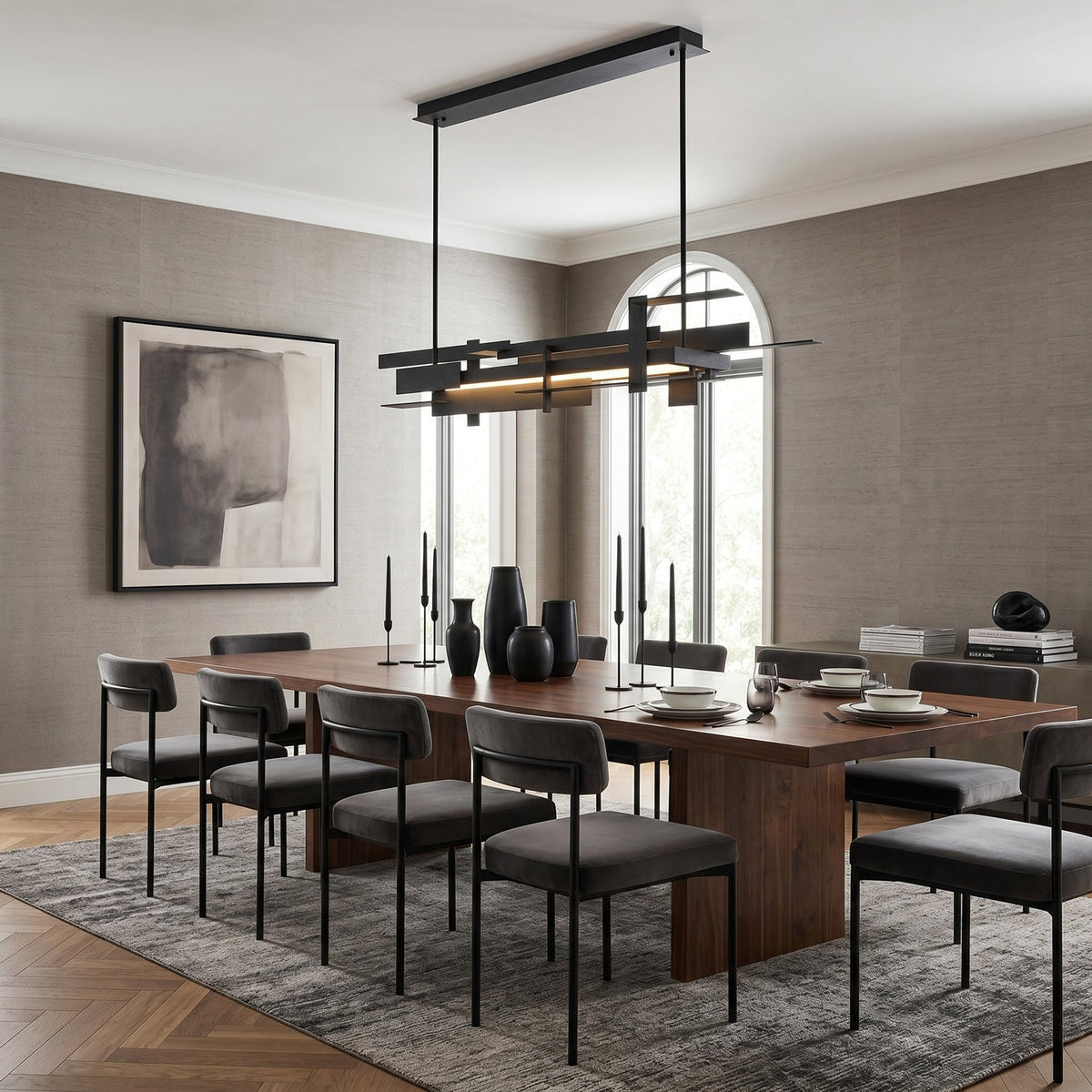 A long matte black Clérachic pendant with layered bars hangs on two rods above a walnut dining table and dark upholstered chairs.