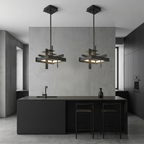 Two compact black geometric Clérachic pendants hang above a black kitchen island with bar stools, against a grey concrete-look wall.