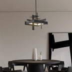 A compact black Clérachic pendant with a stacked-bar frame hangs above a round black dining table, with a large abstract print behind.