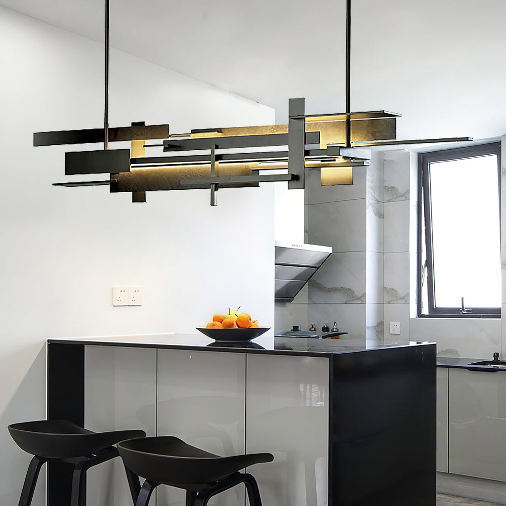 A long Clérachic pendant with layered dark bars hangs in a bright kitchen with a black island, fruit bowl and two black stools.