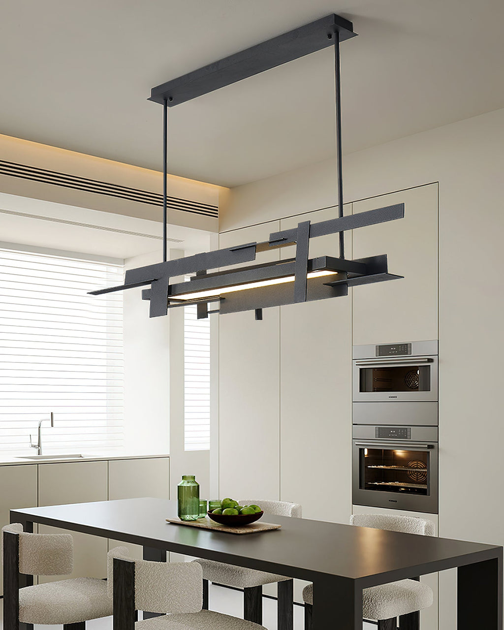 A linear black Clérachic pendant hangs above a black dining table in a white kitchen with built-in ovens and a warm ceiling glow.