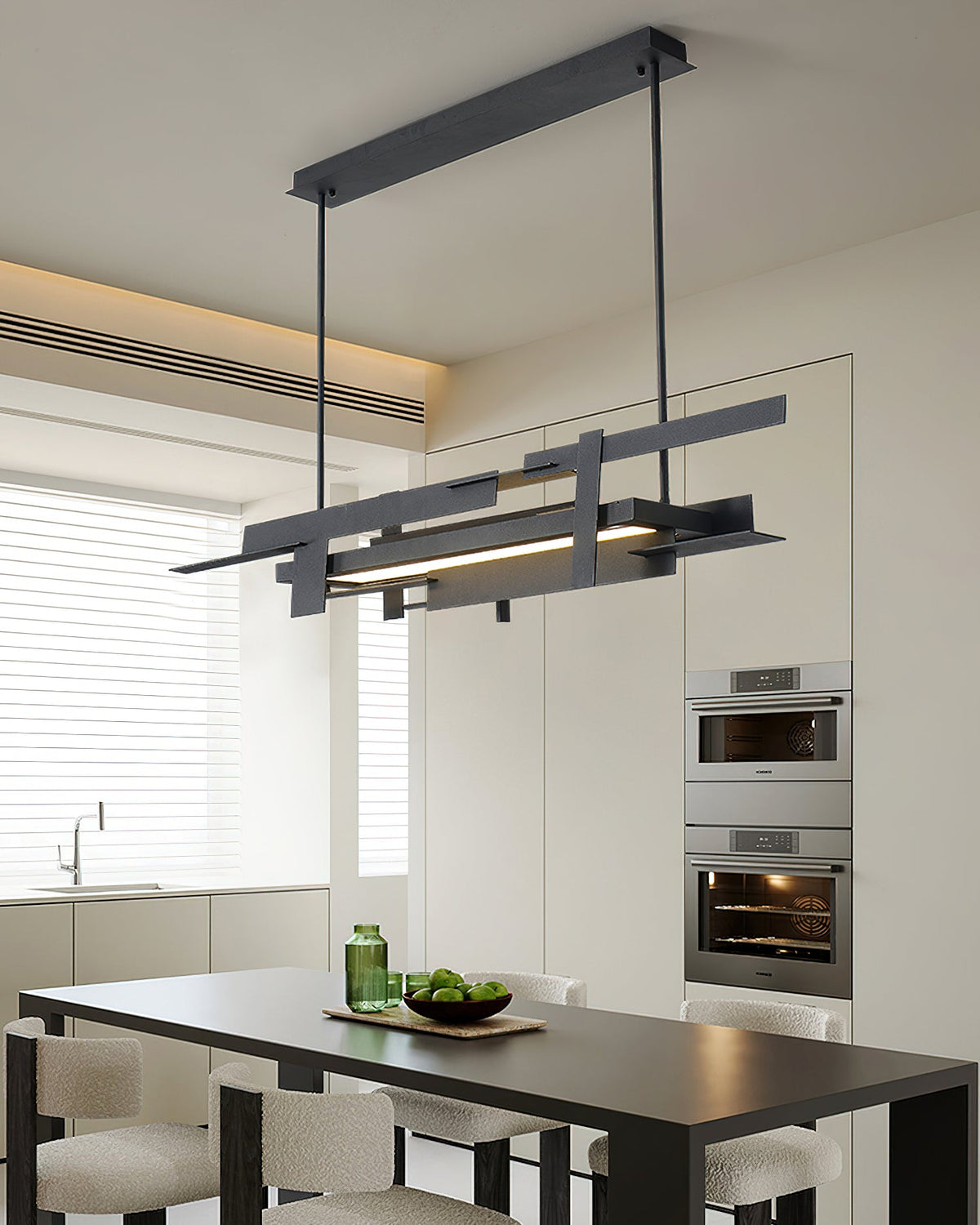 A linear black Clérachic pendant hangs above a black dining table in a white kitchen with built-in ovens and a warm ceiling glow.