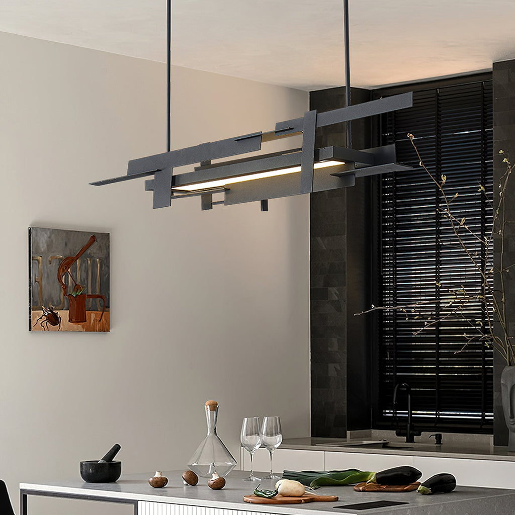 A black linear Clérachic pendant with a lit bar hangs in a dark-shuttered kitchen, with glasses and a carafe on the counter.