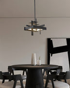 A compact black Clérachic pendant hangs on a single rod above a round dark table with black chairs, in front of a grey wall.