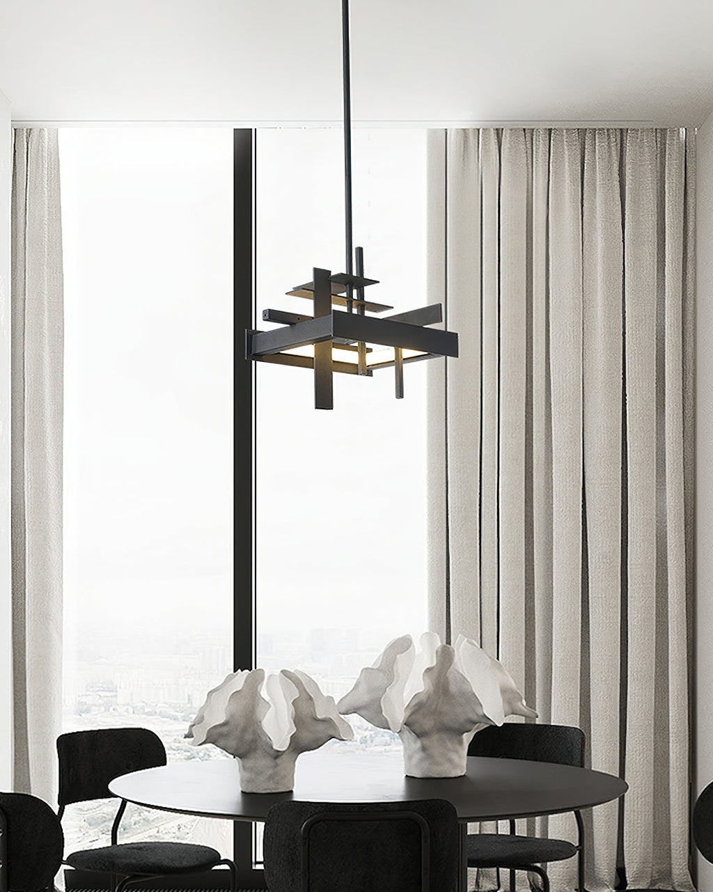 A compact black Clérachic pendant hangs in front of tall windows and sheer curtains, above a round table with sculptural white ornaments.