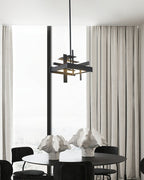 A compact black Clérachic pendant hangs in front of tall windows and sheer curtains, above a round table with sculptural white ornaments.