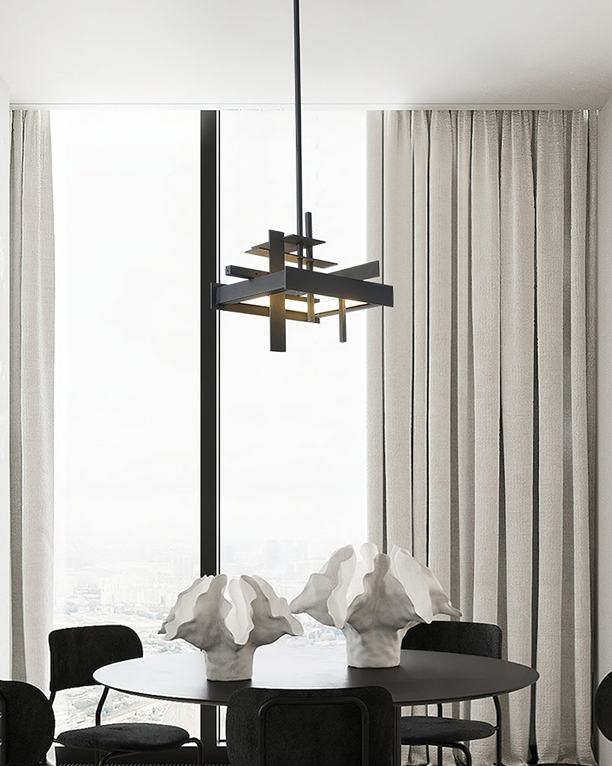 A compact black Clérachic pendant hangs in front of tall windows and sheer curtains, above a round table with sculptural white ornaments.