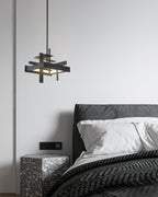 A compact black Clérachic pendant hangs on a single rod beside a dark bed with white pillows and a terrazzo bedside table.