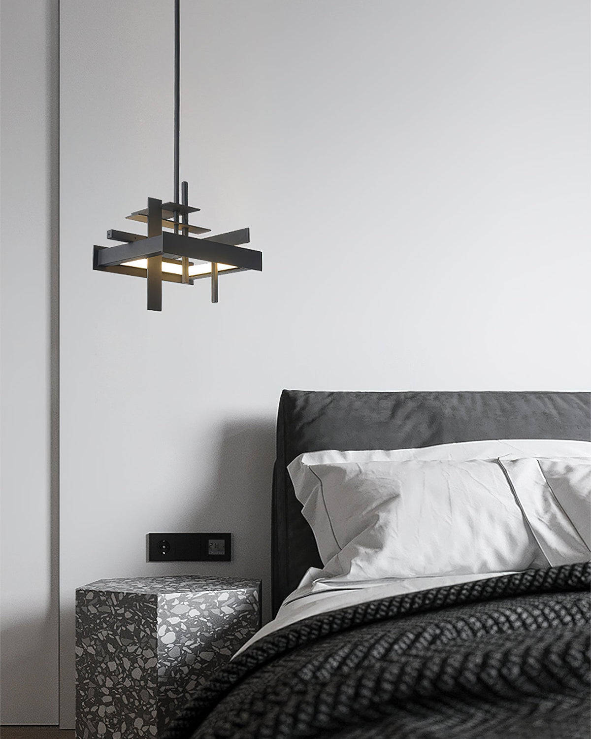 A compact black Clérachic pendant hangs on a single rod beside a dark bed with white pillows and a terrazzo bedside table.