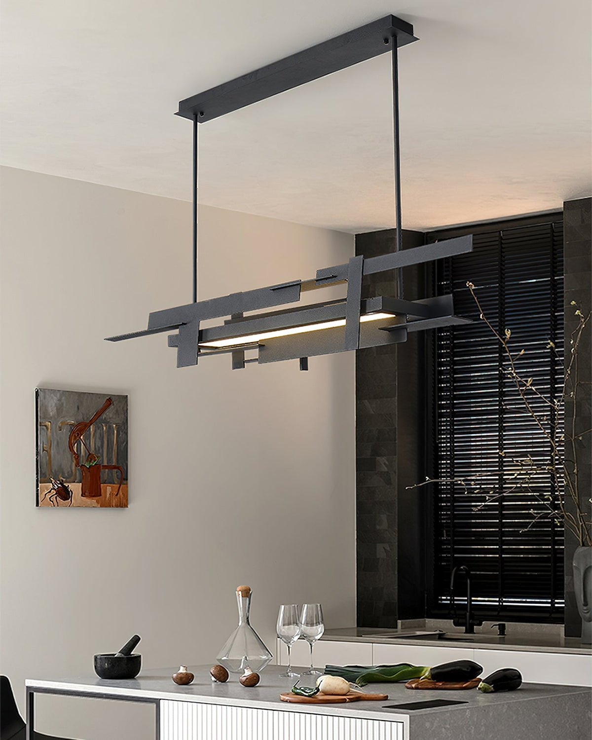A linear matte black Clérachic pendant on a ceiling bar hangs above a kitchen counter, with a dark shutter and a glass carafe beside it.