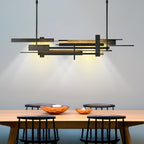 A wide dark Clérachic pendant with layered bars throws warm light down onto a timber table with copper bowls and black spindle chairs.