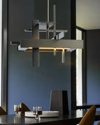 Close view of a dark, textured Clérachic pendant with stacked bars and a warm glow, above a dark table and a blue wall.