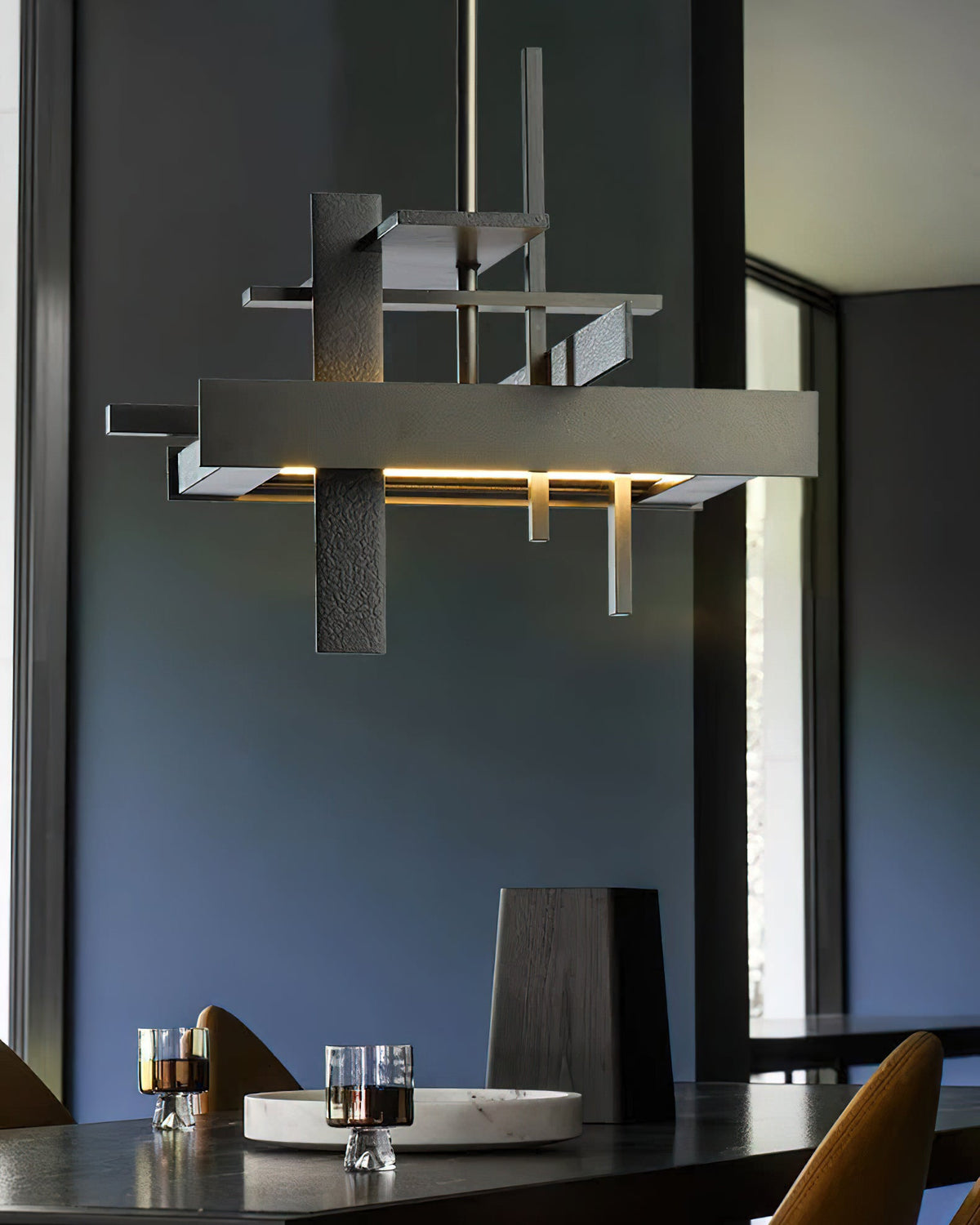 Close view of a dark, textured Clérachic pendant with stacked bars and a warm glow, above a dark table and a blue wall.