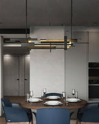 A long dark Clérachic pendant with layered bars hangs in a grey dining room above a round table set with plates and glasses.