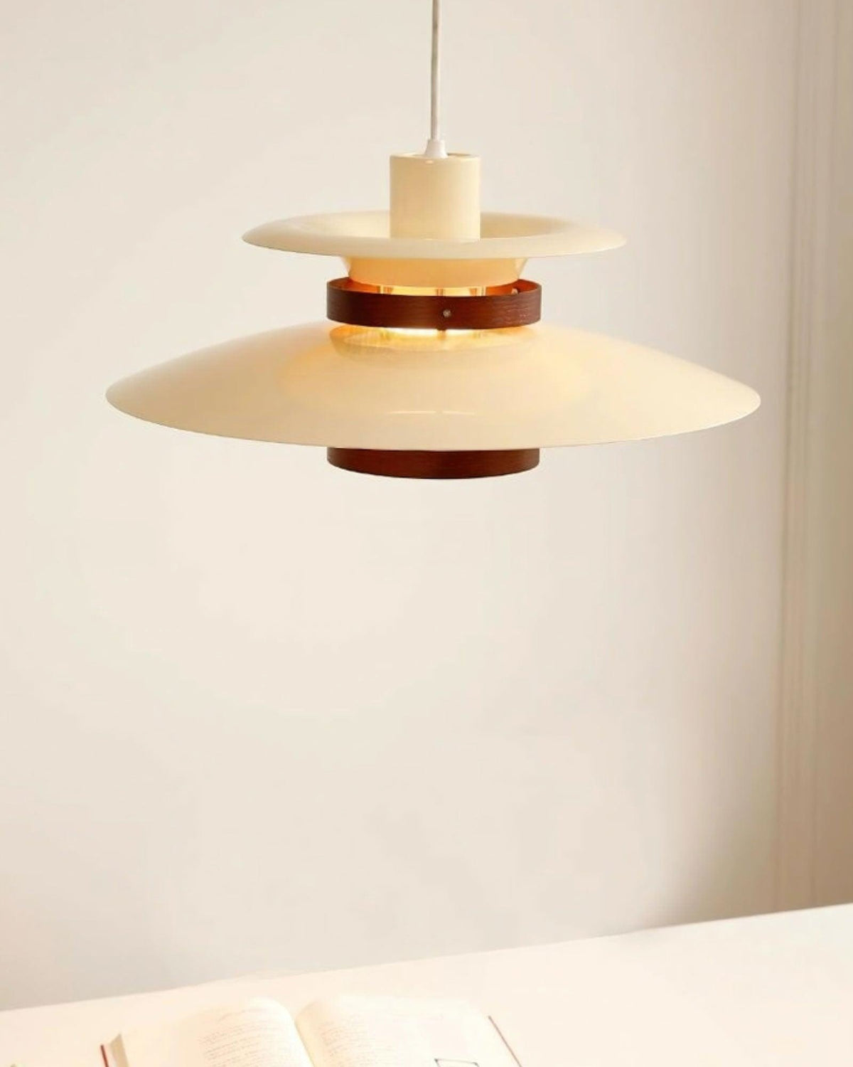A beige Clérachic pendant hangs above an open book on a plain wall.