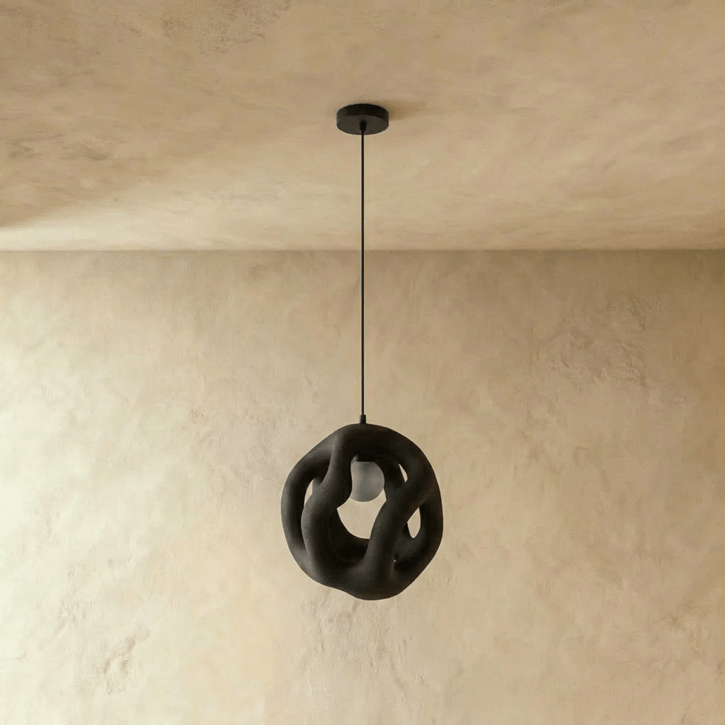 Clérachic black openwork pendant light hanging unlit from a black canopy, its organic looping form against a plaster wall.