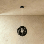 Clérachic black openwork pendant light hanging unlit from a black canopy, its organic looping form against a plaster wall.