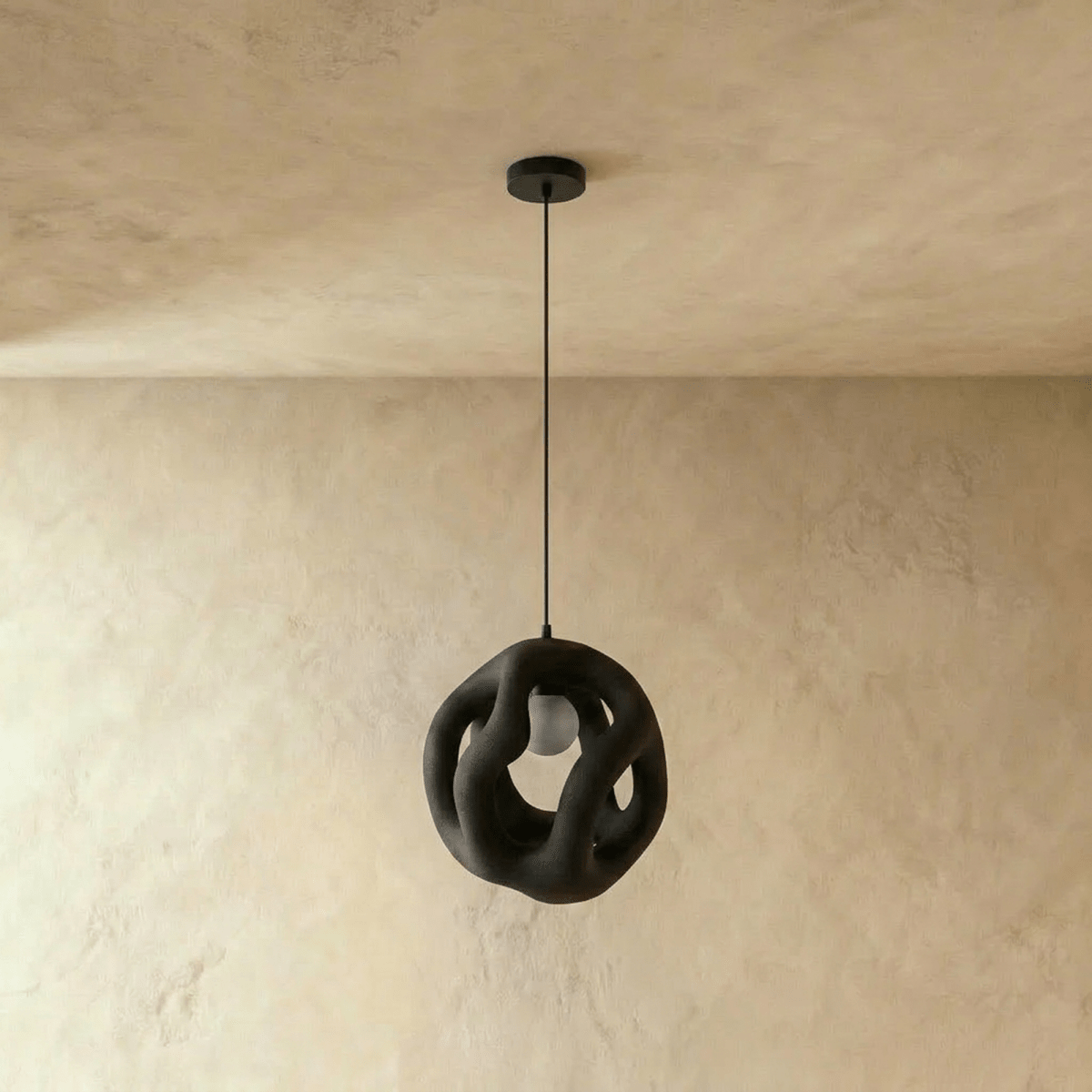 Clérachic black openwork pendant light hanging unlit from a black canopy, its organic looping form against a plaster wall.